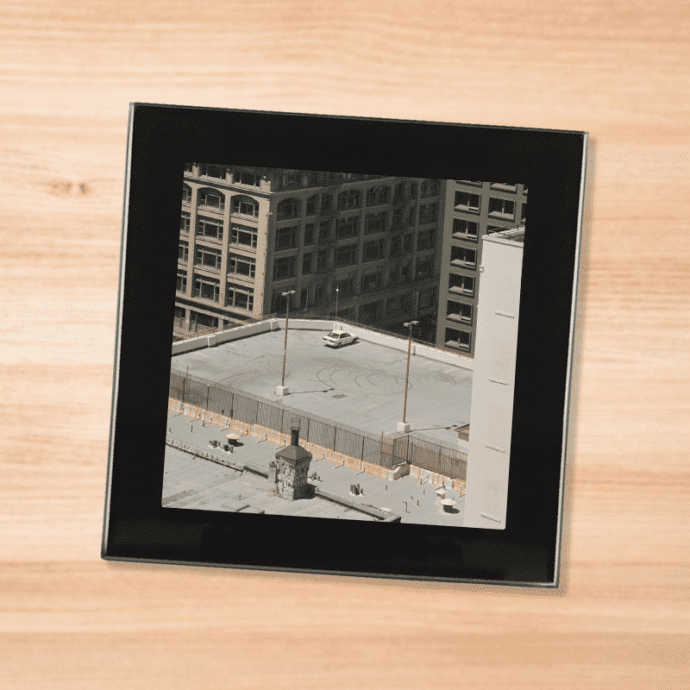 Black glass Arctic Monkeys album coaster on a wood table