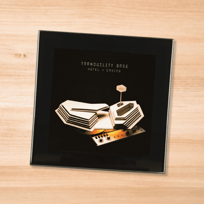Black glass Arctic Monkeys album coaster on a wood table