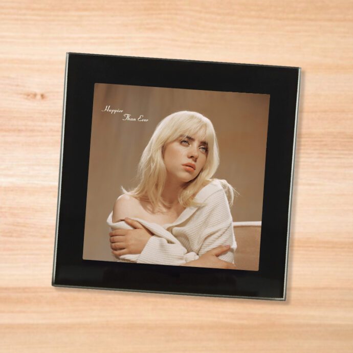 Black glass Billie Eilish - Happier Than Ever coaster on a wood table
